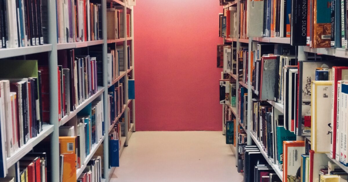 ピンクの壁と本棚が並ぶ図書館の通路