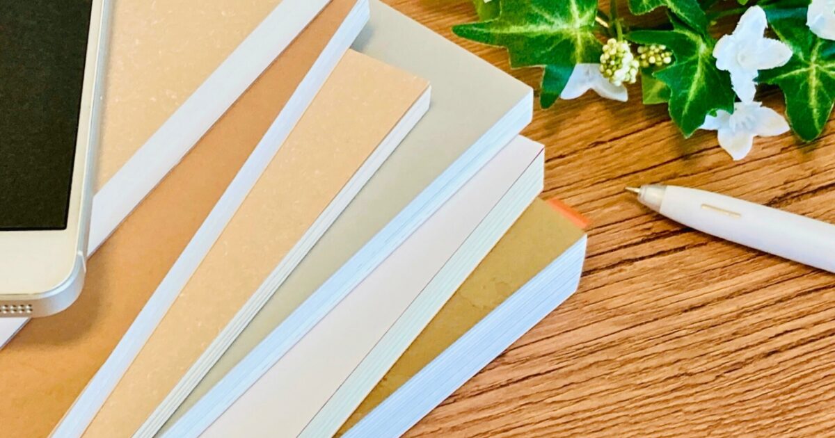 机の上に積まれた本とスマートフォンとペン